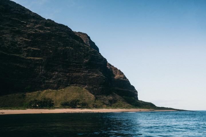 Rocky cliff by a calm ocean under clear blue sky.