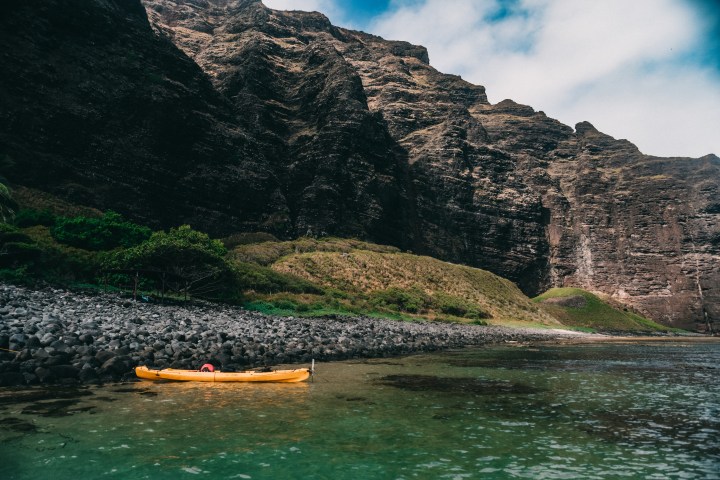 Yellow kayak on calm water near rocky cliffs and greenery under blue sky.