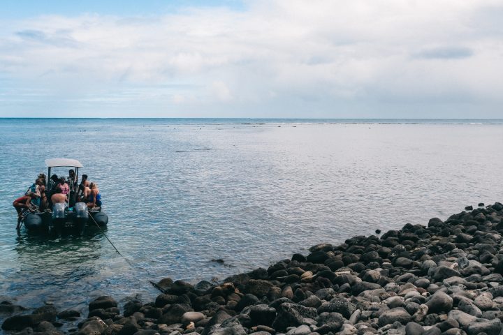 Boat with people near rocky shore on a calm sea under a partly cloudy sky.