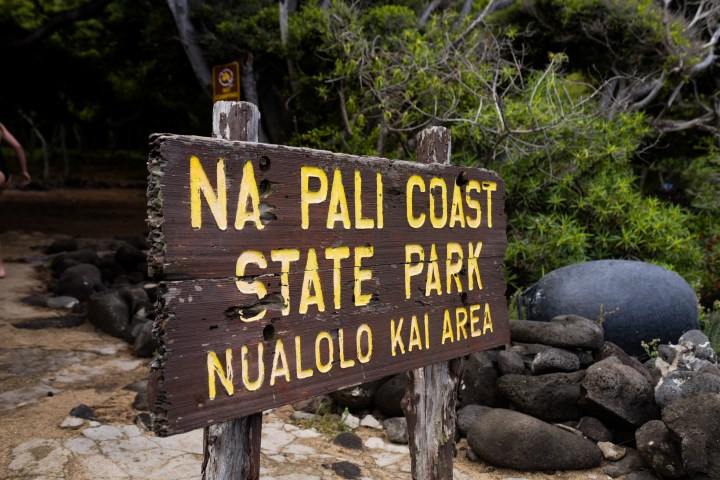 Wooden sign at Na Pali Coast State Park entrance with rocky background.