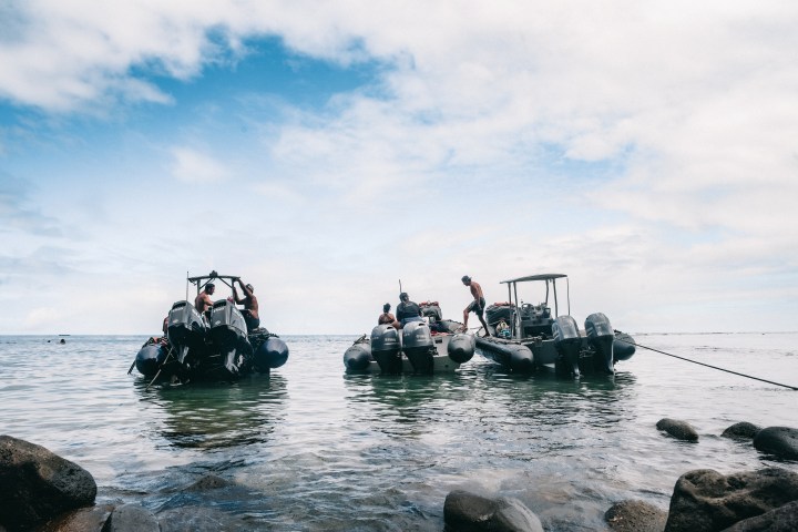 People on inflatable boats near a rocky shore under cloudy sky.