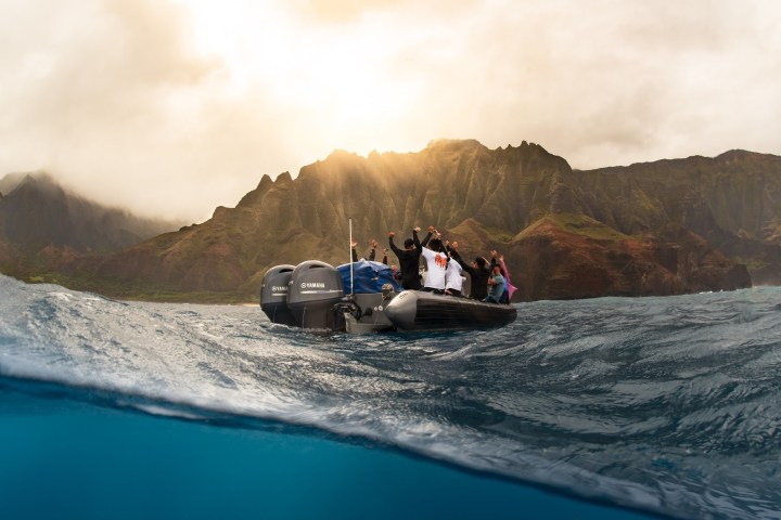 a man riding on the back of a boat next to a mountain