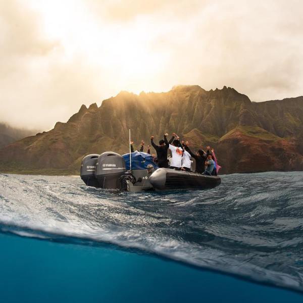 rafting tours on the Na Pali Coast in Kauai with Kauai Sea Tours. Group of people in raft having fun and surrounded by waves and a beautiful view