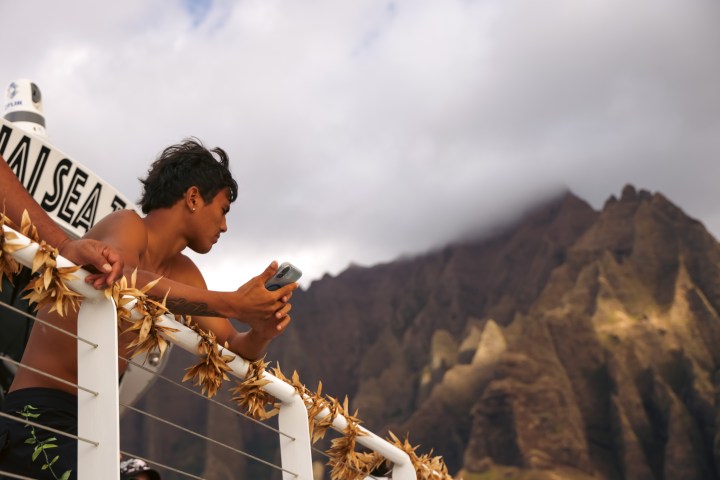 Person leaning on boat railing with mountains in the background.