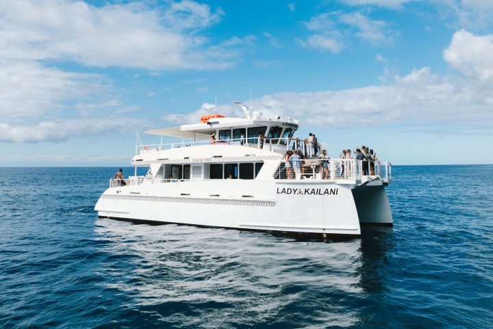 White catamaran named Lady Kailani with people onboard sailing in open sea under a blue sky with clouds.