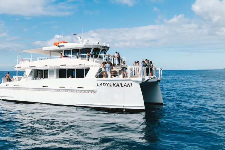 White catamaran named Lady Kailani with people onboard sailing in open sea under a blue sky with clouds.