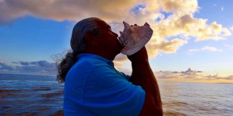 man_blowing_conch_shell_client_image_kauai_sea_tours a man standing in front of a body of water