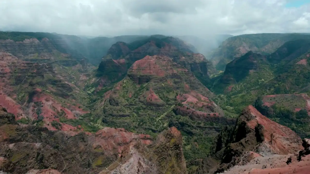 Aerial view of a vast, colorful canyon under a cloudy sky.