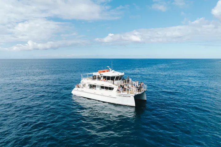 White yacht with tourists on a calm, open ocean under a partly cloudy sky.
