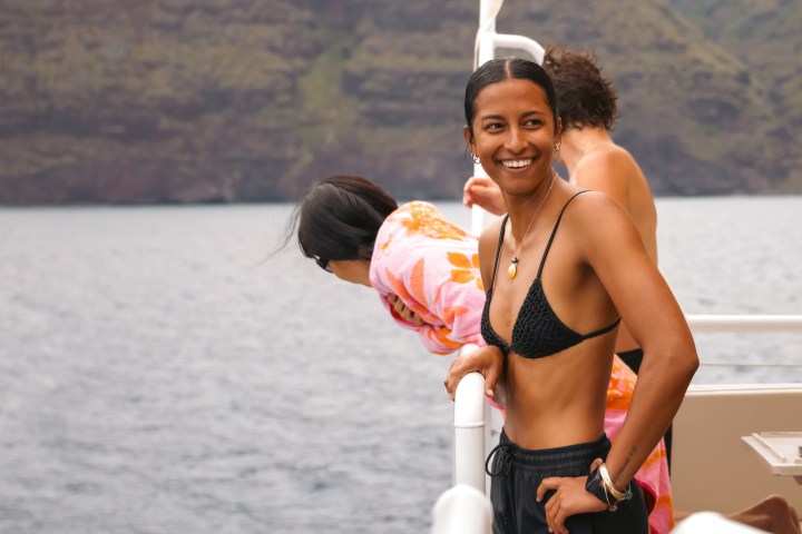 Smiling person in a bikini on a boat, with mountains in the background.