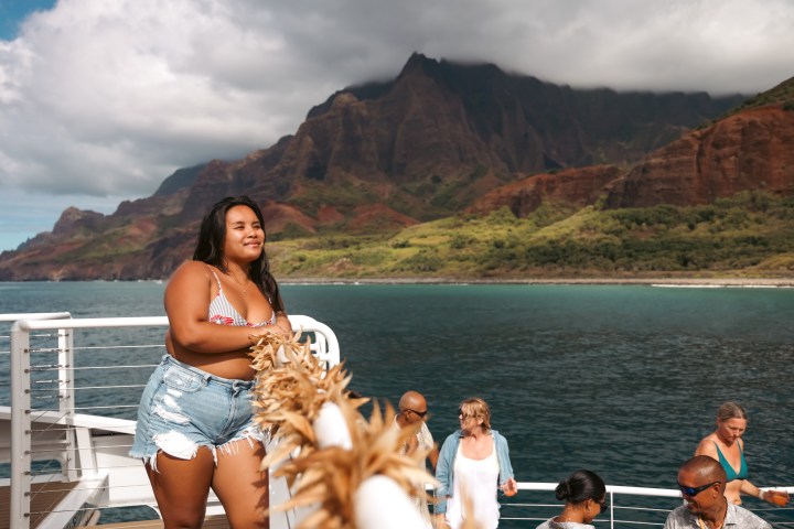 Woman on a boat with mountains and ocean in the background.