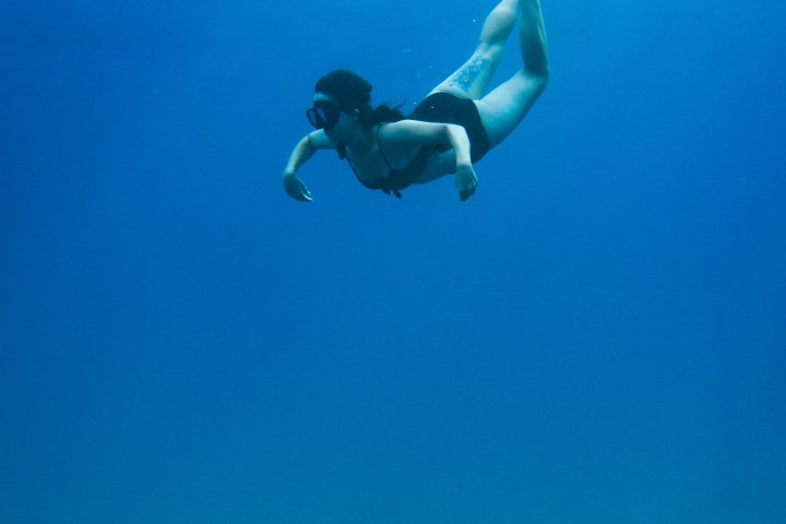 Person snorkeling underwater in blue ocean wearing fins and mask.