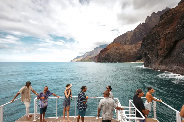 People on a boat enjoy a scenic view of cliffs and ocean under a cloudy sky.