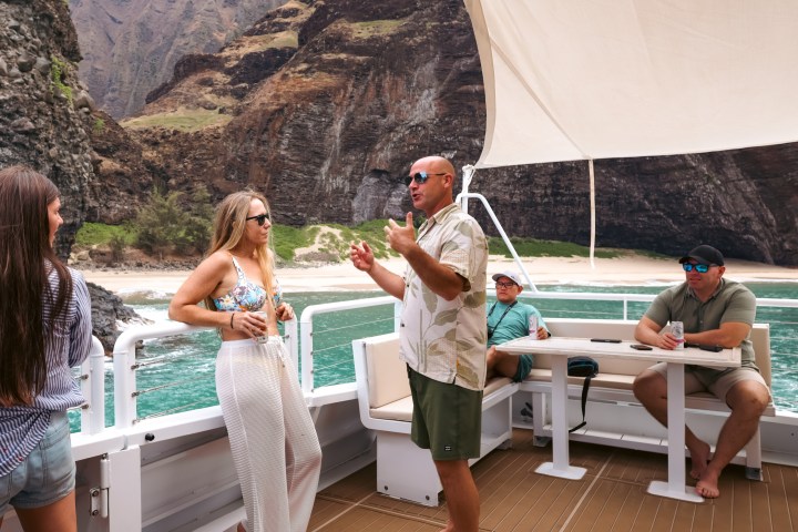 People on a boat talking, mountainous coastline in the background.