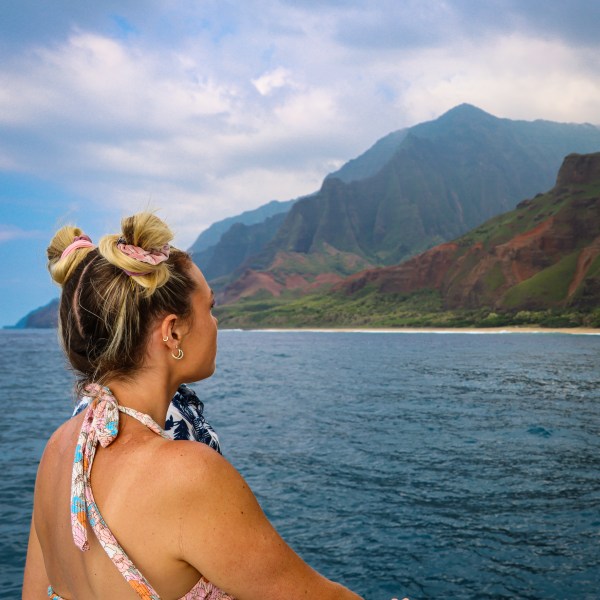 Person on a boat looking at a mountainous coastline under a cloudy sky.