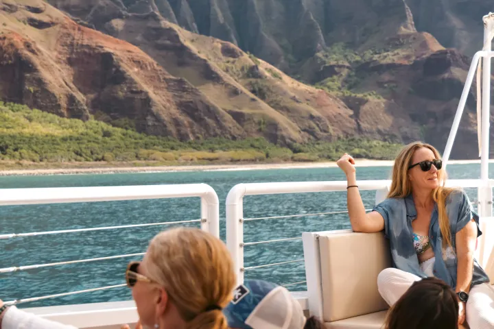 People relaxing on a boat with scenic mountainous coastline in the background.