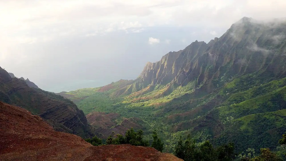Dramatic mountain range with lush green valleys under a cloudy sky.