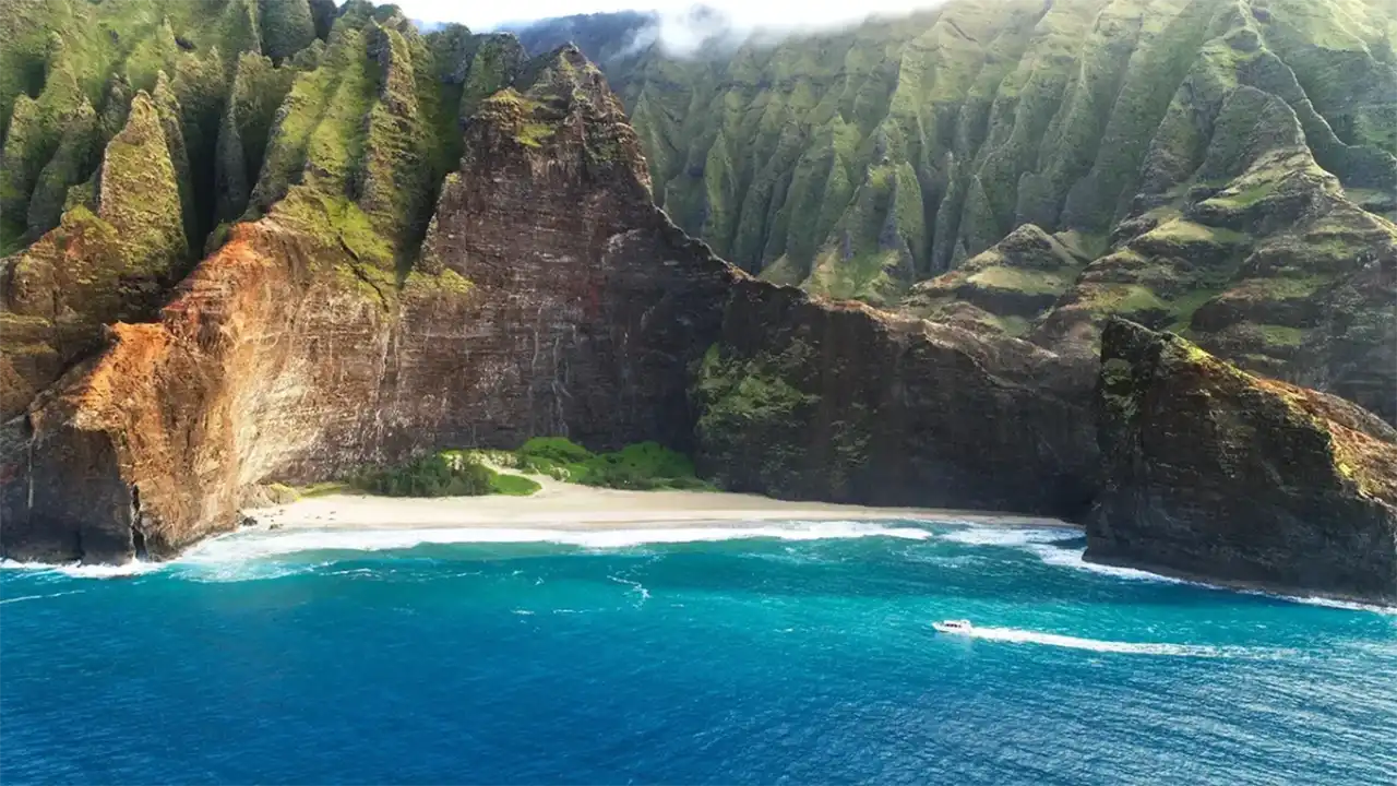 Aerial view of a beach with steep cliffs and lush green mountains.