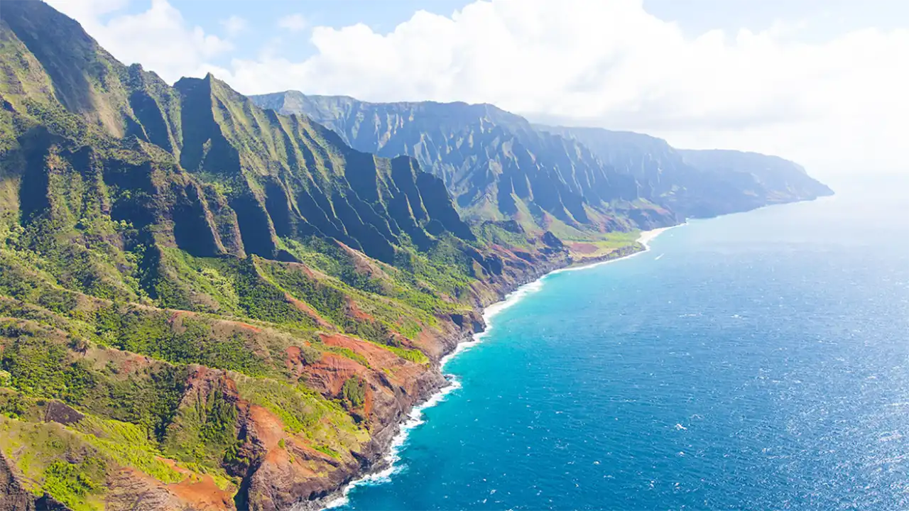Aerial view of a coastal mountain range with cliffs and turquoise ocean.