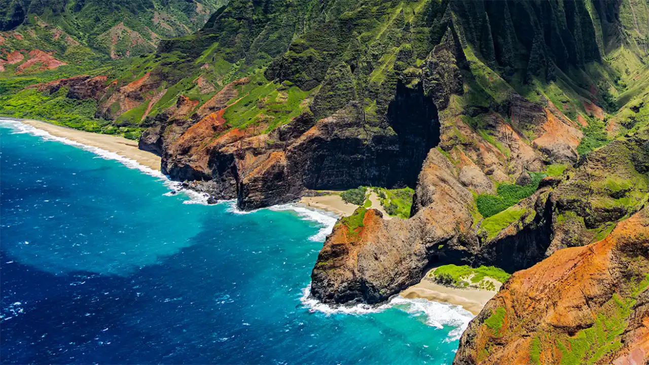 Aerial view of a coastal landscape with cliffs, green vegetation, and blue ocean.