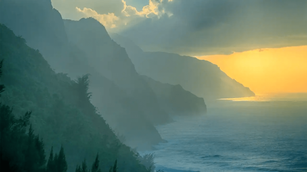 Misty coastal cliffs at sunset with ocean waves and cloudy sky.