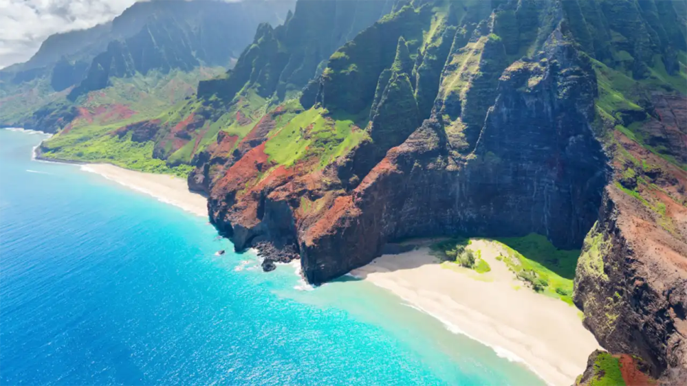 Aerial view of a coastline with cliffs, beach, and turquoise ocean.