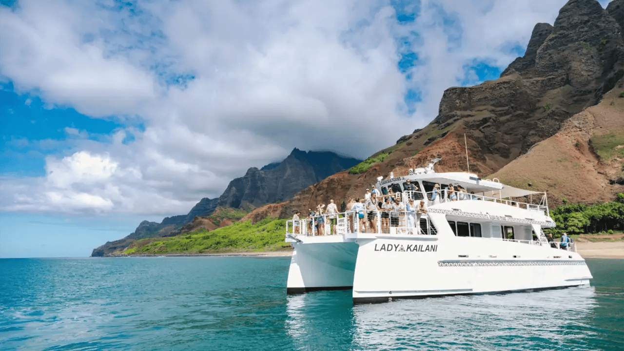 Catamaran near scenic coastline with blue sky and clouds.