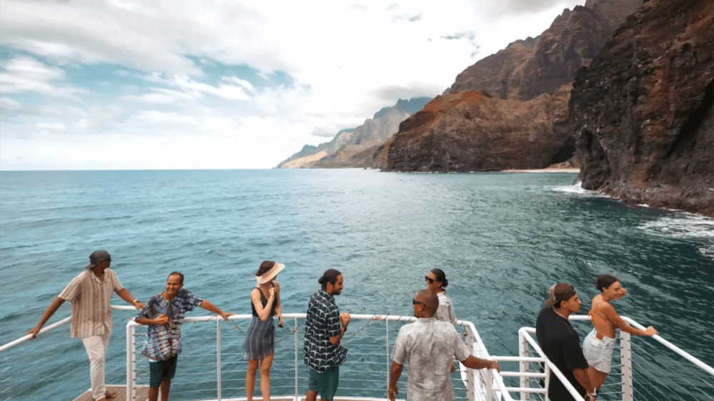 People on a boat admiring rocky coastal scenery under a cloudy sky.